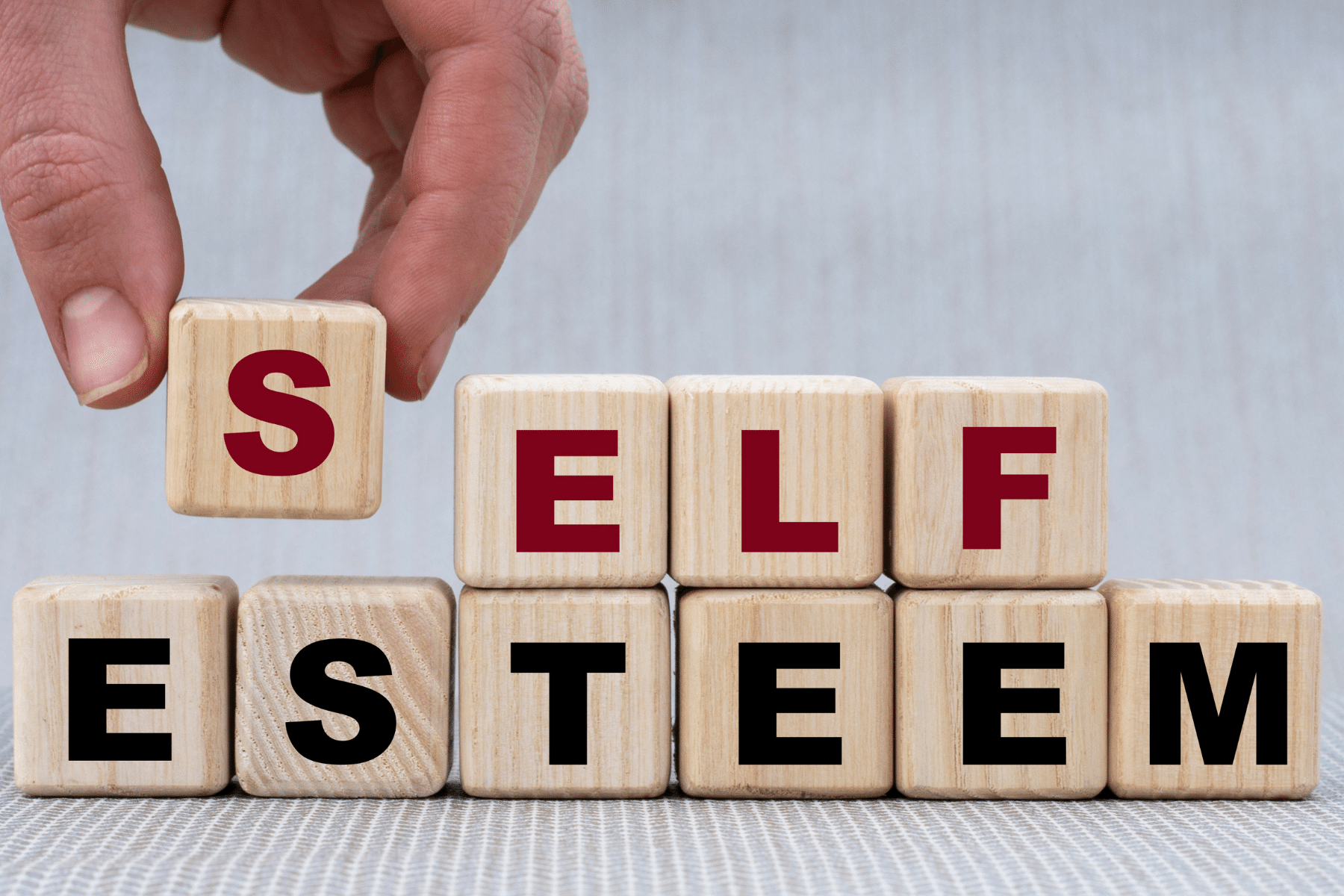 Scrabble letters spelling out the word self-esteem on a light blue background