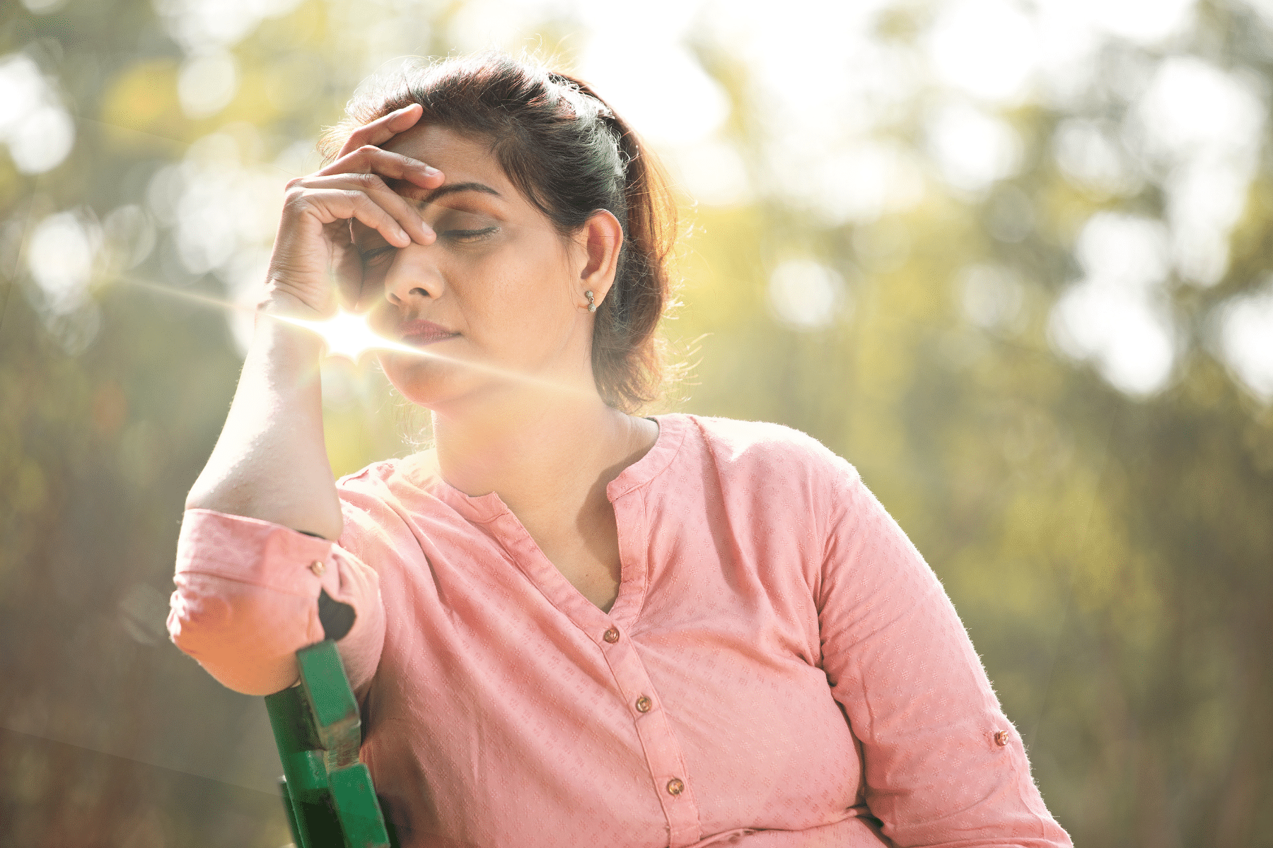 woman with her head down holding her head with the sun shining through